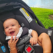 Lunabelle is registered to the contest to win money with this photo: baby, car_seat, child, clothing, cute, daylight, expression, grass, hands, happy, infant, legs, nature, outdoor, park, person, safety, seatbelt, smiling, water_fountain