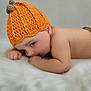 baby, infant, child, knitted_hat, orange, lying_down, fluffy_surface, cute, soft_texture, skin, portrait, indoors, sleepwear, newborn, cozy, warm, small_hands, resting, headwear, peaceful
