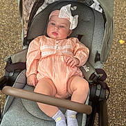Adriana joined the competition — help win amazing prizes! baby, child, stroller, peach_outfit, white_bow, gray_stroller, socks, outdoor, infant, cute, seated, baby_clothing, headband, soft_lighting, plush, person, portrait, small_child, baby_toddler, casual
