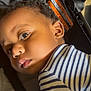 child, baby, face, striped_shirt, curly_hair, lying_down, stroller, car_seat, expression, closeup, portrait, young_child, indoor, clothing, person, head, skin, eyes, infant, baby_boy