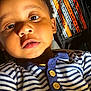baby, child, face, striped_shirt, buttons, closeup, portrait, warning_label, text, light, shadow, skin, eyes, mouth, hair, clothing, infant, cute, indoors, expression