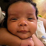 Messiah is registered to the contest to win money with this photo: baby, close_up, face, smiling, arm, curly_hair, skin, child, infant, resting, cute, portrait, happy, person, indoors, young_child, expression, head, hand, cozy