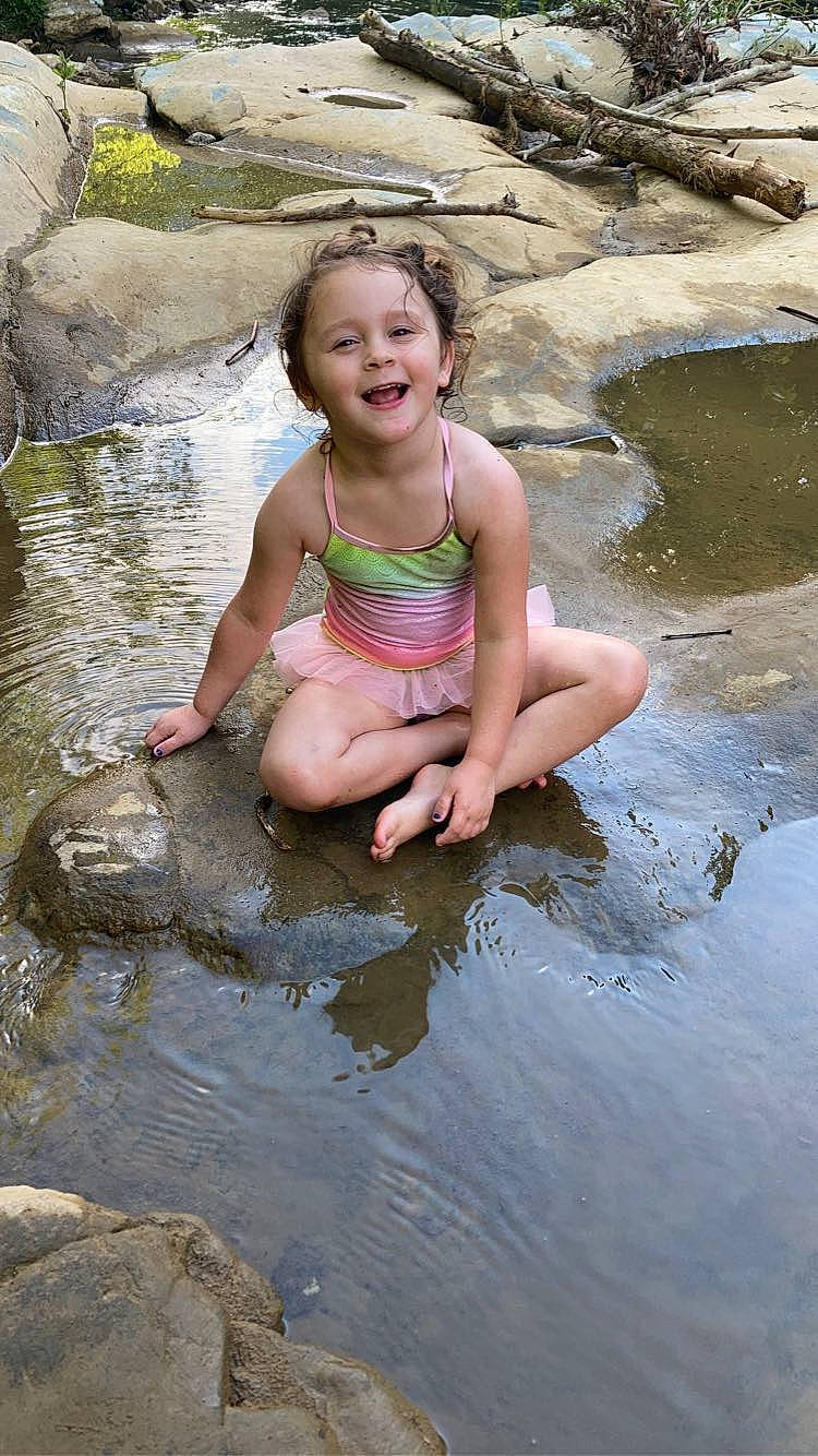 Emma is registered to the contest to win money with this photo: barefoot, bathing, child, foot, fun, hand, happy, joy, leisure, people_in_nature, person, puddle, recreation, reflection, rock, sitting, smile, stream, swimwear, toddler