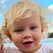 Tippa is registered to the contest to win money with this photo: toddler, child, blonde_hair, curly_hair, blue_eyes, smiling, face, outdoor, sky, clouds, water, white_shirt, earrings, portrait, young_child, cute, happy, person, natural_light, closeup
