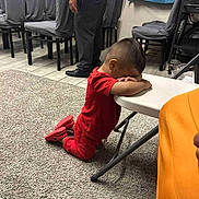 Mateo joined the competition — help win amazing prizes! child, red_clothing, kneeling, carpet, table, indoor, person, adult, chairs, floor_tiles, carpeted_area, cover_chairs, casual, resting, side_view, home, quiet_moment, furniture, room, shoes