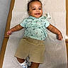baby, child, infant, smiling, happy, portrait, lying_down, indoor, changing_mat, clothing, shirt, shorts, socks, pacifier, furniture, wood, wall, textured_background, photography, adorable