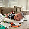 baby, smiling, tummy_time, couch, cushion, toy, curly_hair, indoor, window_blinds, striped_clothing, play_mat, happy, child, infant, face, head, person, soft_toys, blanket, home