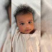 Arthur Augustus is registered to the contest to win money with this photo: baby, infant, child, portrait, face, eyes, curly_hair, smiling, lying_down, blanket, soft, clothing, onesie, indoor, close_up, adorable, head, skin, photography, cozy