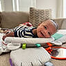 baby, smiling, tummy, striped_clothing, play_mat, mirror, colorful_tags, indoor, couch, pillows, window_blinds, soft_toys, child, happy, face, head, infant, home, person, cute