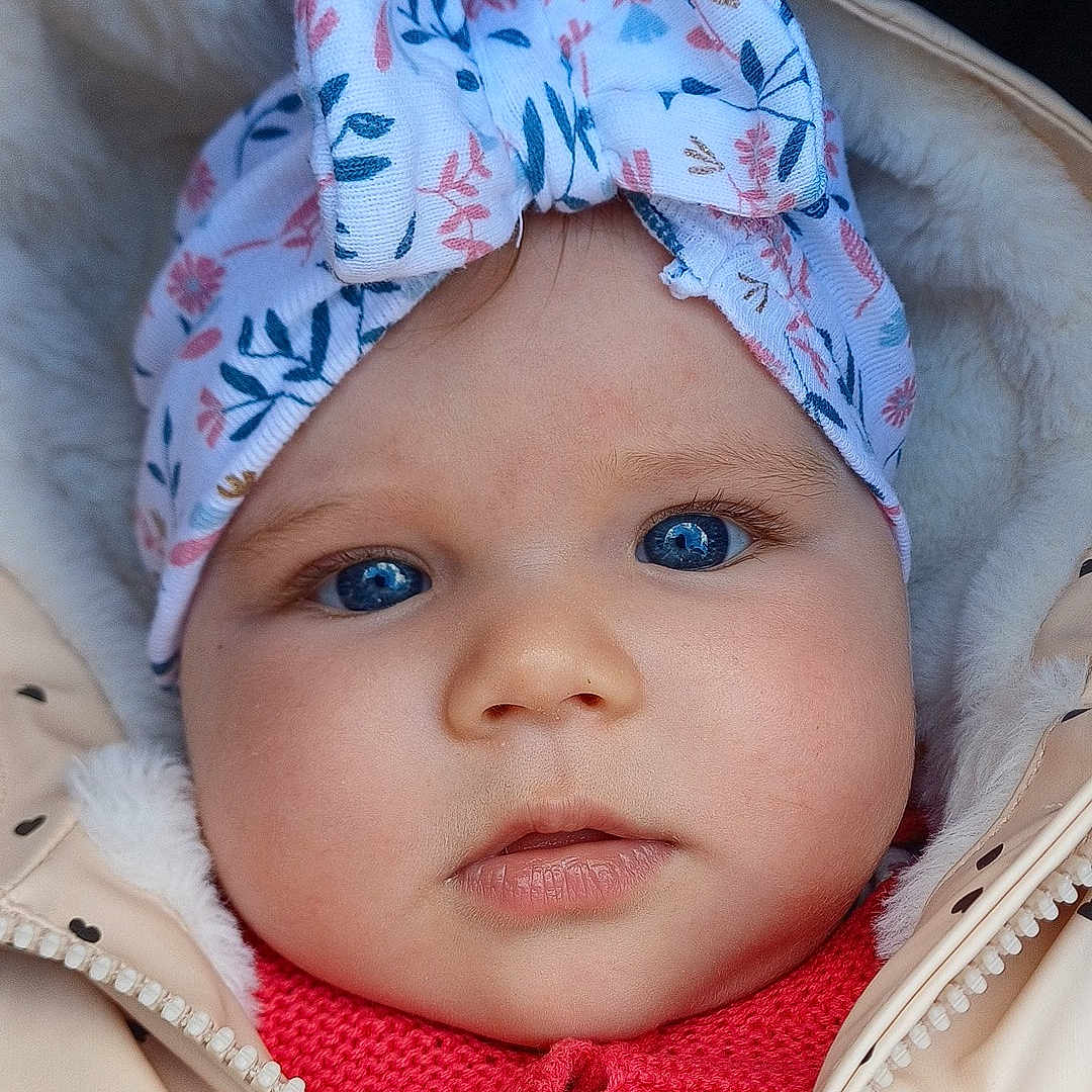 Ambre participe au concours pour gagner de l'argent avec cette photo : baby, child, face, headband, blue_eyes, jacket, red_sweater, cute, portrait, close_up, warm_clothing, infant, outdoor, expression, headwear, bow, soft_texture, skin, young_child, winter
