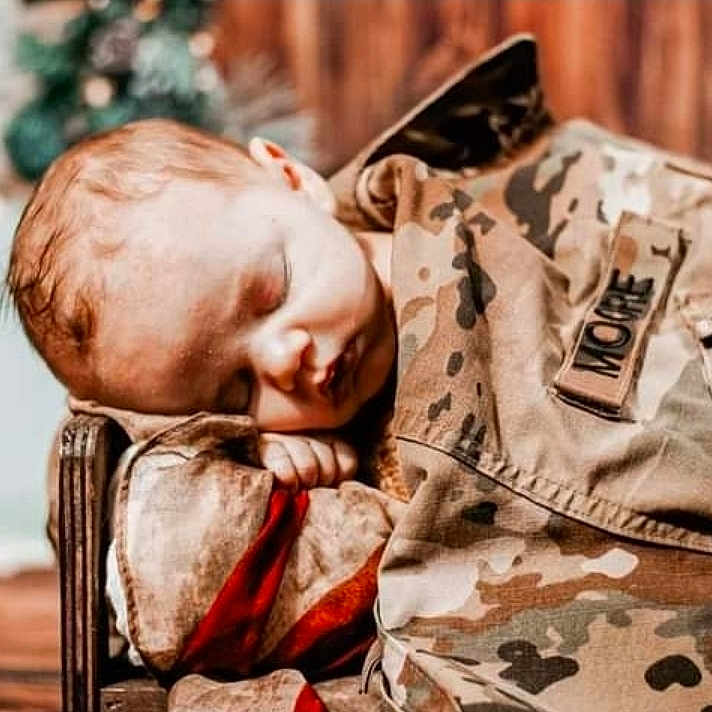 Kal is registered to the contest to win money with this photo: baby, biting, face, head, hugging, military, militaryuniform, officer, person, sleeping, soldier