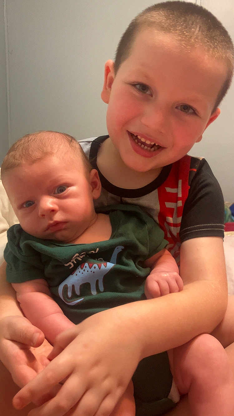 Hunter is registered to the contest to win money with this photo: baby, child, smiling, holding, dinosaur_onesie, infant, portrait, indoor, siblings, cute, happy, person, face, young, toddler, candid, family, skin, arms, expression
