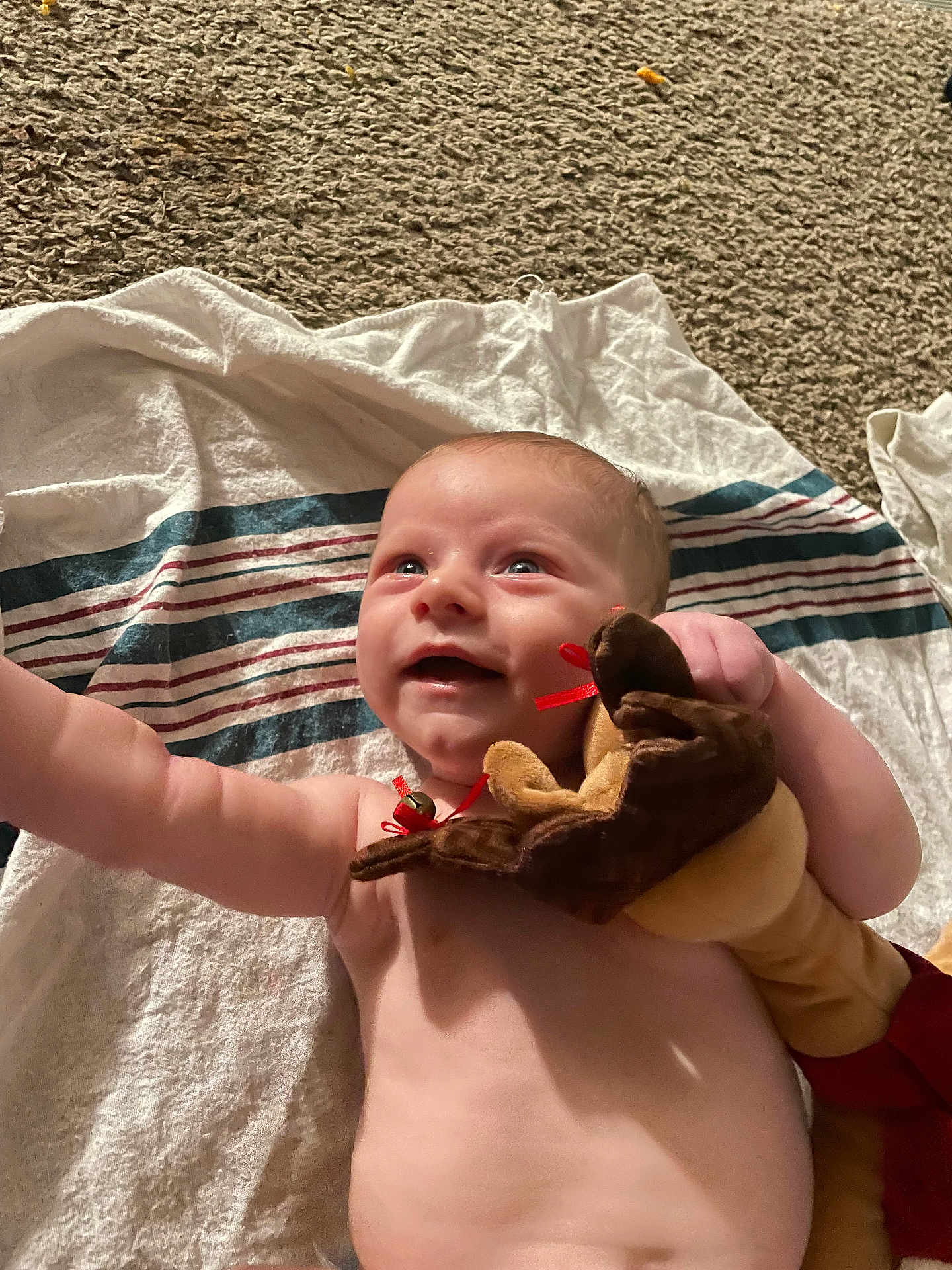 Eric joined the competition — help win amazing prizes! baby, infant, smiling, plush_toy, towel, striped, skin, arm, hand, face, happy, blue_eyes, lying_down, carpet, indoor, child, cute, soft_toy, reaching, joyful