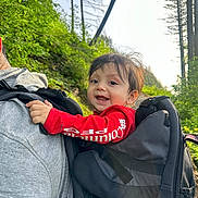 Josiah joined the competition — help win amazing prizes! baby, backpack, bag, clothing, coat, face, grass, head, jacket, land, nature, outdoors, pants, person, photography, plant, portrait, tree, vegetation, woodland