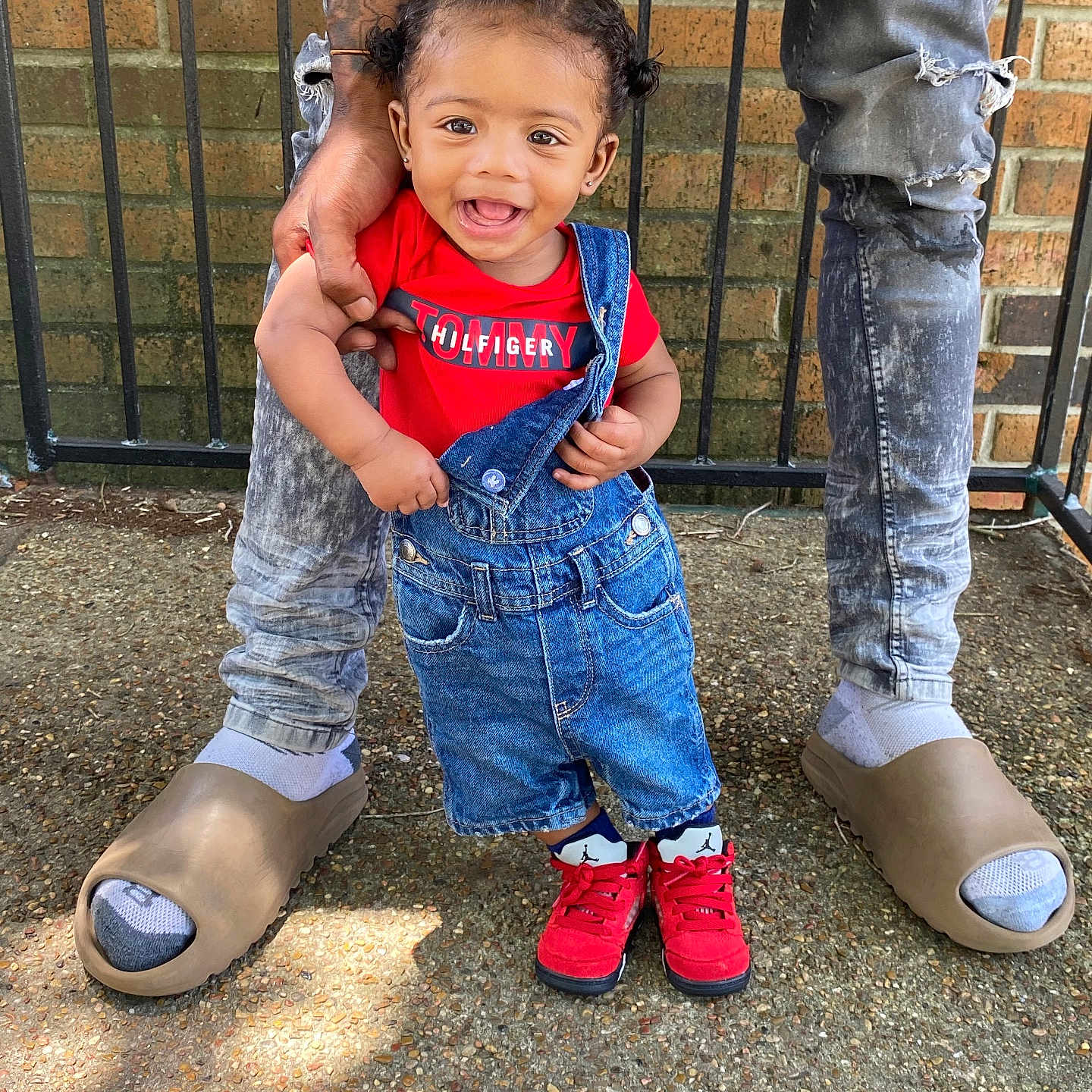 Jaylin Jr joined the competition — help win amazing prizes! adult, brick_wall, casual, child, concrete_ground, denim_overalls, fashion, happy, holding_hand, metal_fence, outdoor, person, portrait, red_shirt, red_shoes, ripped_jeans, smiling, socks, tattoo, toddler