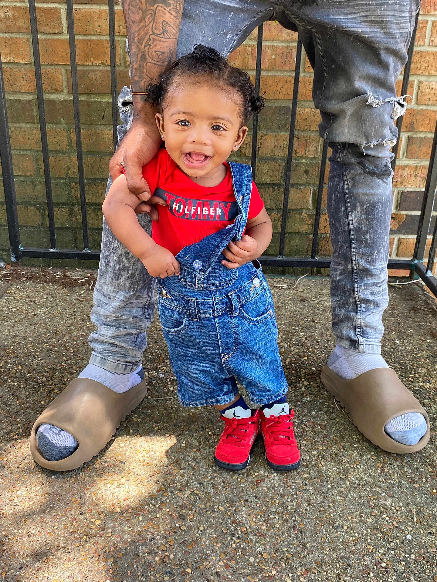 Jaylin Jr joined the competition — help win amazing prizes! toddler, child, smiling, red_shirt, denim_overalls, adult, tattoo, ripped_jeans, red_shoes, socks, outdoor, concrete_ground, metal_fence, brick_wall, happy, person, fashion, casual, holding_hand, portrait