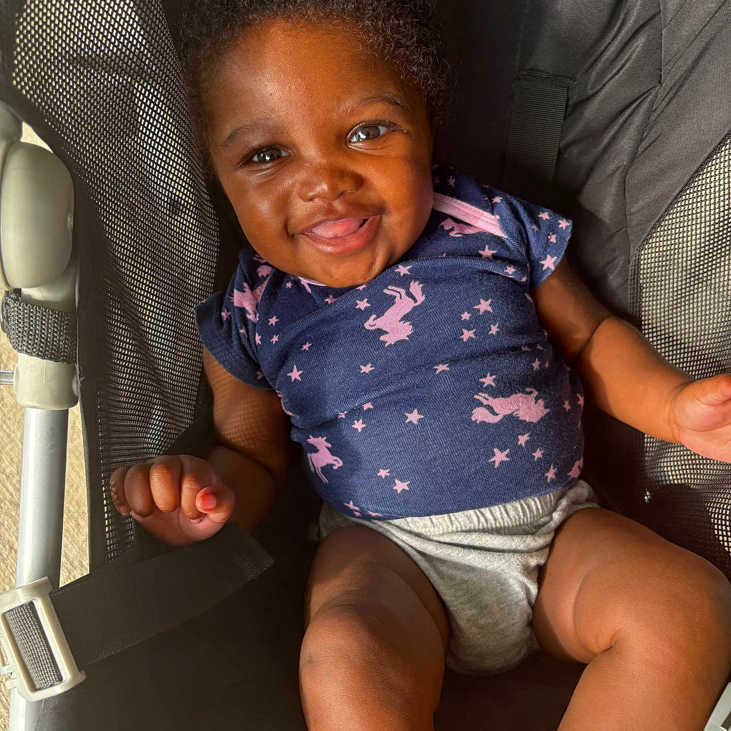 Eloni is registered to the contest to win money with this photo: baby, baby_clothing, blue_shirt, cheerful, child, cute, hands, happy, indoors, infant, legs, maclaren, mesh_fabric, portrait, seatbelt, shorts, smiling, stroller, sunlight, unicorn_pattern