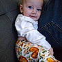 baby, child, person, jeans, couch, clothing, white_top, patterned_pants, pumpkin_pattern, floral_pattern, face, smile, indoor, seated, cozy, snuggling, cute, comfort, portrait, casual