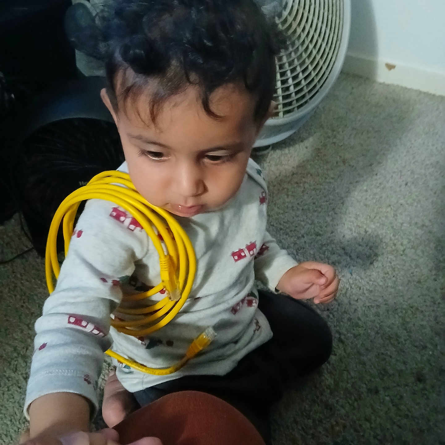 Kultej joined the competition — help win amazing prizes! toddler, child, curly_hair, yellow_cable, hand_holding, carpet, fan, remote_control, indoor, sitting, long_sleeve_shirt, white_shirt, patterned_shirt, person, floor, technology, adult_hand, candid, casual, cute