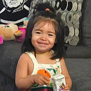 Roxanna is registered to the contest to win money with this photo: toddler, child, juice_box, smiling, sitting, couch, plush_toy, pillow, patterned_cushion, indoor, happy, person, black_and_white_art, hair_tie, tank_top, table, background_art, furniture, cute, portrait