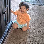 Roxanna joined the competition — help win amazing prizes! toddler, child, smiling, indoor, carpet, cabinet, orange_shirt, blue_shorts, kneeling, person, home, furniture, curly_hair, cute, young_child, happy, playful, candid, baby, portrait