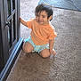 toddler, child, smiling, indoor, carpet, cabinet, orange_shirt, blue_shorts, kneeling, person, home, furniture, curly_hair, cute, young_child, happy, playful, candid, baby, portrait