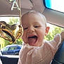 baby, blurred_background, car_interior, charm, child, cute, happy, heart_shaped, outdoor, pendant, person, pink_sweater, playful, rearview_mirror, seat, smiling, steering_wheel, tongue_out, window, young_child