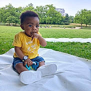 Raphael a rejoint le concours — aidez-le/la à gagner de superbes lots ! toddler, child, outdoor, park, grass, blanket, yellow_shirt, denim_shorts, toy, sitting, greenery, nature, daylight, trees, person, footwear, casual_clothing, cute, curious, baby