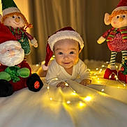 Amélie participe au concours pour gagner de l'argent avec cette photo : baby, santa_hat, christmas, fairy_lights, dolls, toys, smile, blanket, holiday, cute, festive, indoors, child, face, portrait, christmas_decor, happy, infant, soft_lighting, cozy
