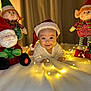 baby, santa_hat, christmas, fairy_lights, dolls, toys, smile, blanket, holiday, cute, festive, indoors, child, face, portrait, christmas_decor, happy, infant, soft_lighting, cozy
