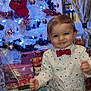 toddler, child, christmas_tree, holiday, presents, bow_tie, festive_clothing, indoor, smiling, decorations, ornaments, lights, white_tree, curtains, window, wooden_floor, celebration, happy, party, cute