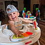 baby, child, smiling, cap, mesh_cap, striped_shirt, activity_center, toy, piano_keys, indoor, living_room, wooden_floor, furniture, playtime, happy, person, infant, cute, colorful, baby_toys
