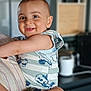 baby, child, smiling, person, holding, arms, striped_clothing, cartoon_print, indoor, blurred_background, face, head, cute, happy, infant, young_child, short_hair, light_skin, portrait, toddler