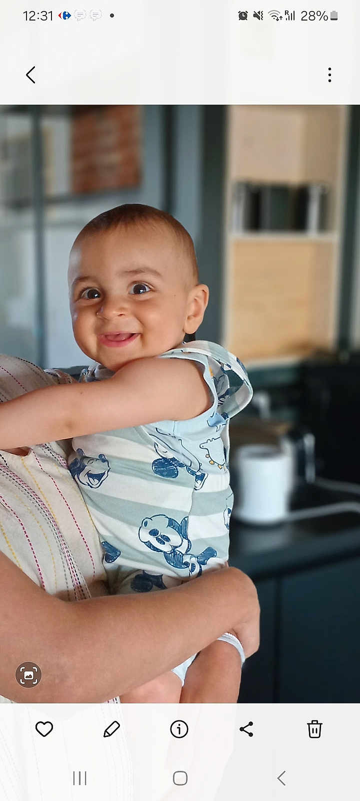 Noham a rejoint le concours — aidez-le/la à gagner de superbes lots ! baby, child, smiling, person, holding, arms, striped_clothing, cartoon_print, indoor, blurred_background, face, head, cute, happy, infant, young_child, short_hair, light_skin, portrait, toddler