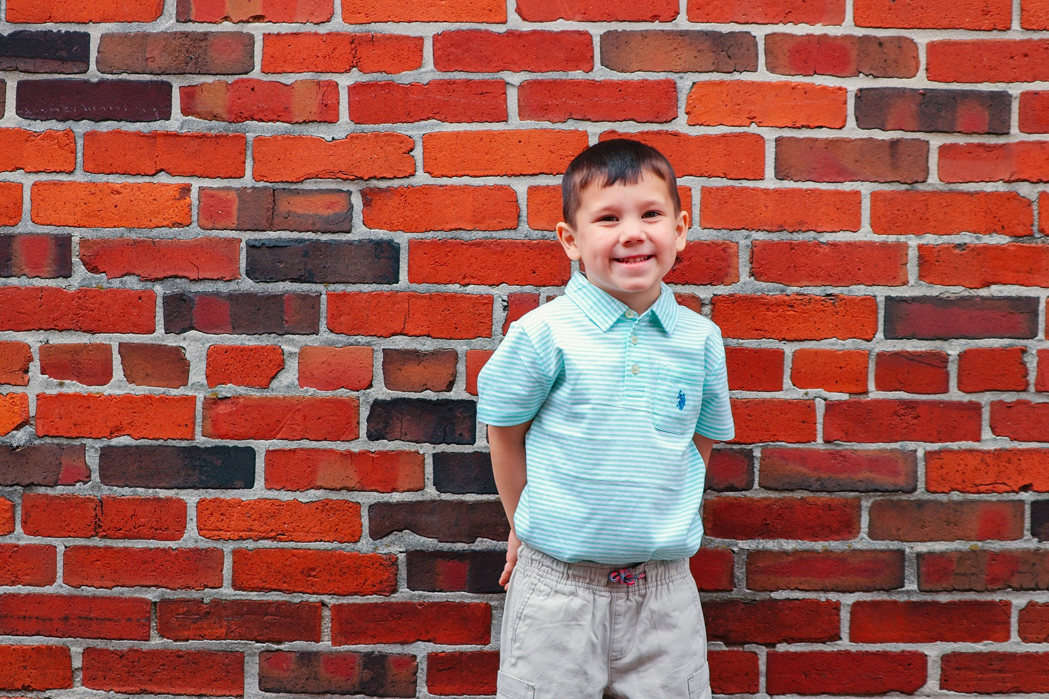Kenzie James is registered to the contest to win money with this photo: brick, brickwork, child, chin, electric_blue, facial_expression, hair, hairstyle, happy, head, joy, pattern, person, photograph, rectangle, red, sleeve, smile, standing, t_shirt
