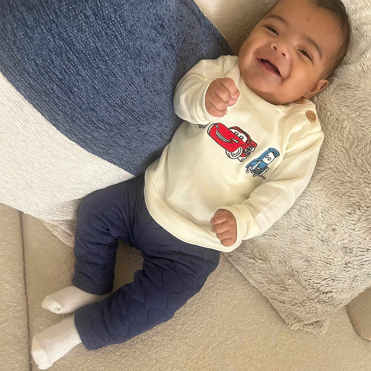 Eiden is registered to the contest to win money with this photo: baby, blue_pants, cartoon_cars, child, couch, cozy, cream_sweater, cute, happy, indoor, infant, person, pillow, portrait, relaxed, seated, smiling, soft_fabric, white_socks, young_child