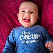 Taho participe au concours pour gagner de l'argent avec cette photo : baby, blanket, blue_clothing, child, cozy, cute, eyes, face, french_text, hand, happy, indoors, infant, laughing, lying_down, magenta_background, mouth_open, portrait, smiling, soft_texture