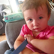 Layla joined the competition — help win amazing prizes! baby, child, infant, portrait, close_up, pink_shirt, blue_toy, toy, sitting, chair, indoors, home, brown_hair, serious_expression, looking_at_camera, hands, arms, playroom, furniture, natural_light