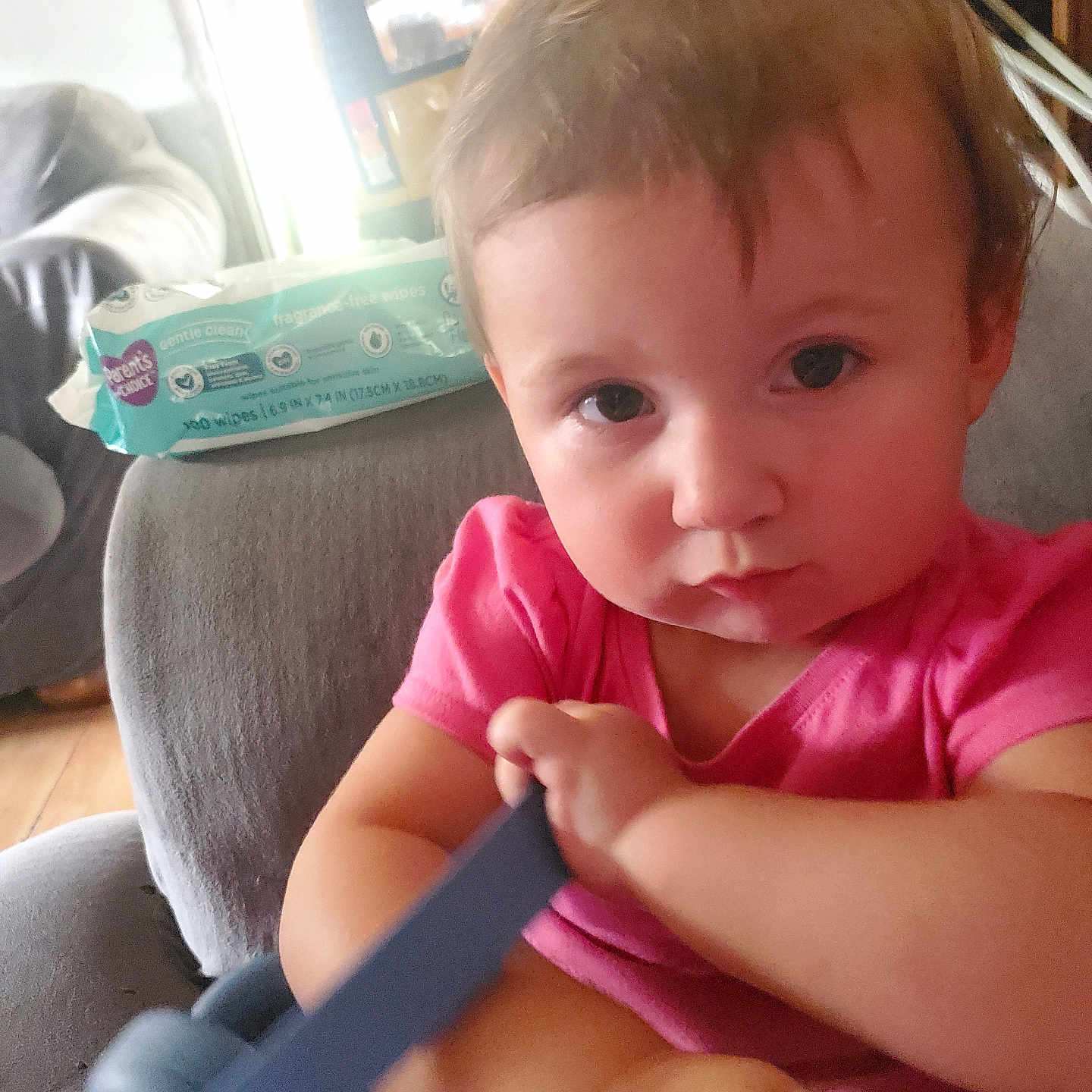 Layla joined the competition — help win amazing prizes! baby, child, infant, portrait, close_up, pink_shirt, blue_toy, toy, sitting, chair, indoors, home, brown_hair, serious_expression, looking_at_camera, hands, arms, playroom, furniture, natural_light