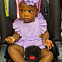baby, child, car_seat, purple_outfit, headband, flower, white_socks, frilly_socks, black_car_seat, infant, cute, portrait, seated, looking_away, indoors, adorable, clothing, person, young_child, expression