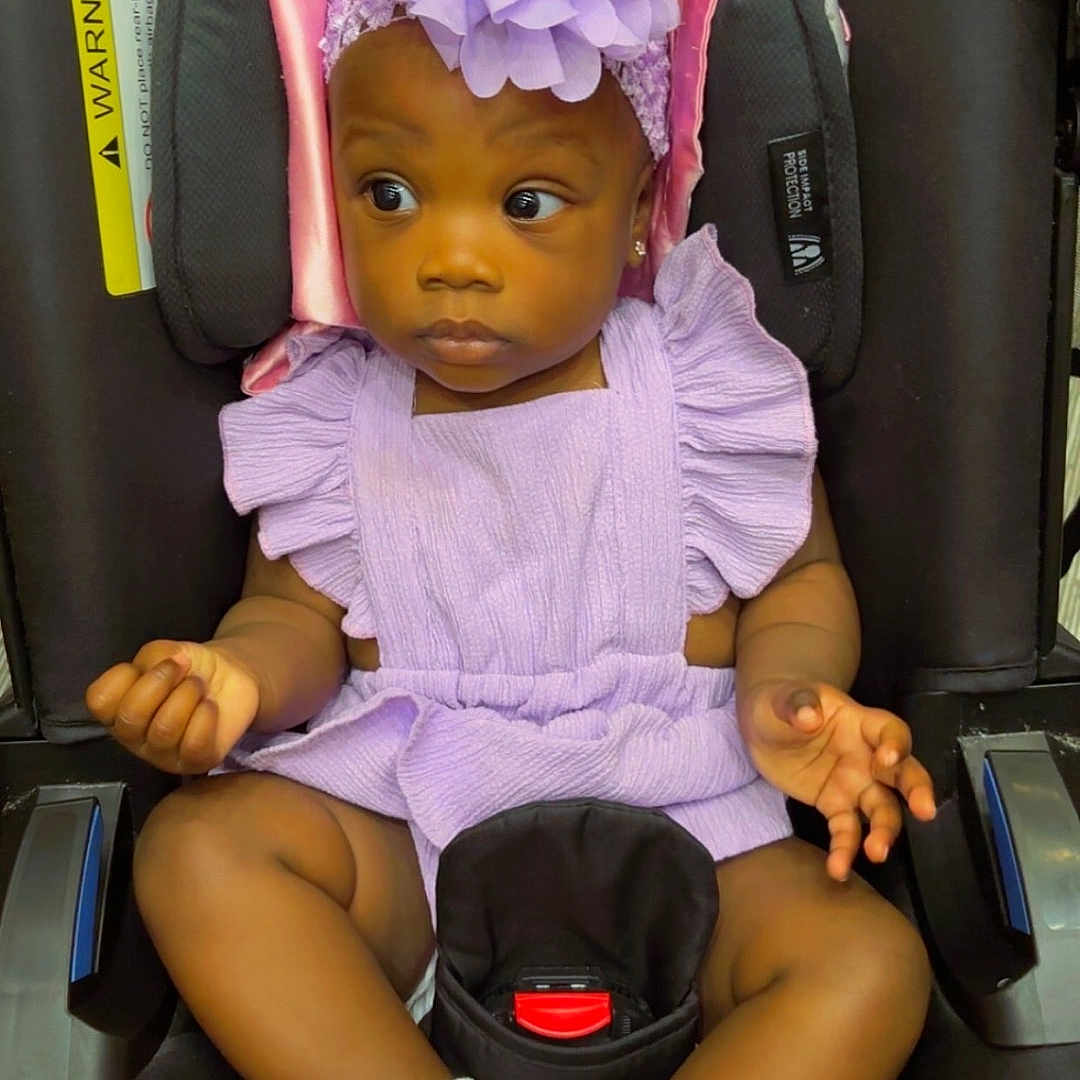 Jailee is registered to the contest to win money with this photo: adorable, baby, black_car_seat, car_seat, child, clothing, cute, expression, flower, frilly_socks, headband, indoors, infant, looking_away, person, portrait, purple_outfit, seated, white_socks, young_child