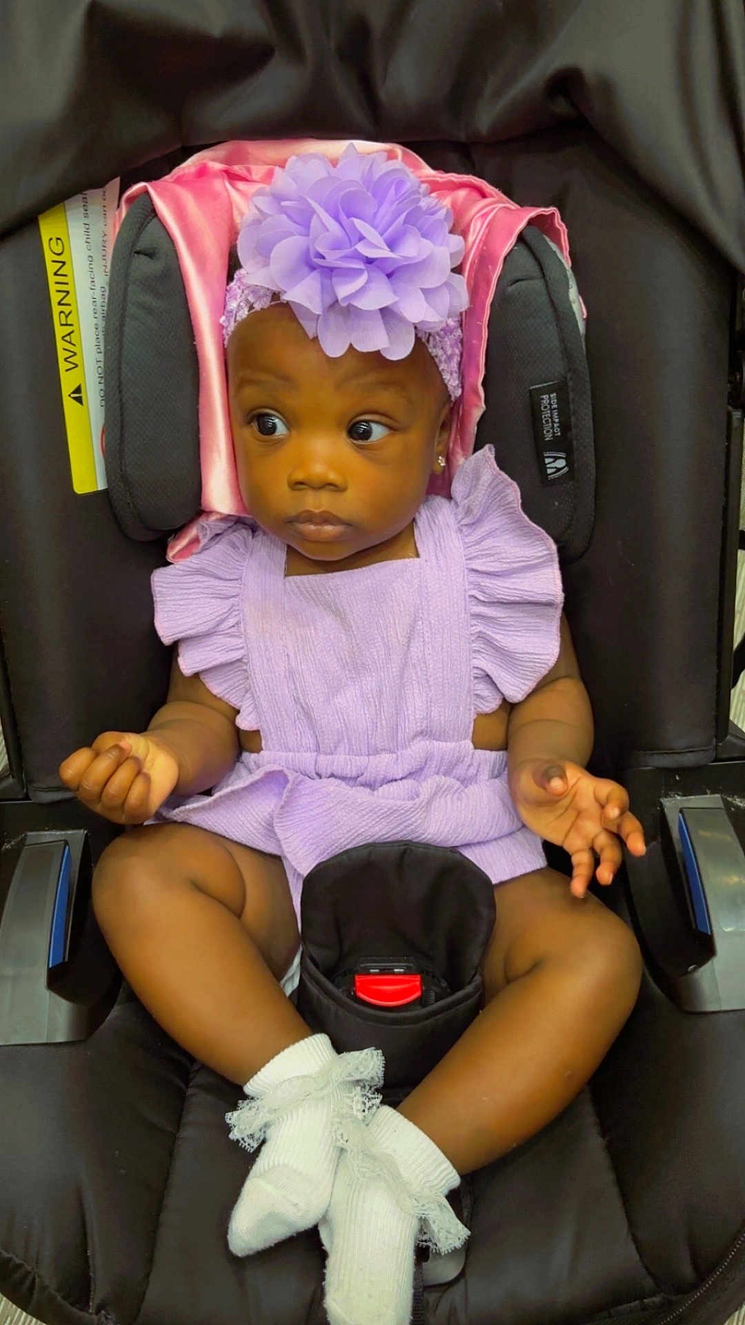 Jailee is registered to the contest to win money with this photo: baby, child, car_seat, purple_outfit, headband, flower, white_socks, frilly_socks, black_car_seat, infant, cute, portrait, seated, looking_away, indoors, adorable, clothing, person, young_child, expression