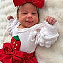 baby, infant, newborn, bow, red_bow, headband, winking, tongue_out, smiling, white_blanket, cozy_blanket, red_skirt, strawberry_patch, ruffled_sleeves, lying_down, closeup, tiny_hands, soft_texture, portrait, cute