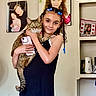 Sprinkles joined the competition — help win amazing prizes! girl, cat, indoor, portrait, child, braids, smartphone, family_photos, shelf, household_items, smile, tabby_cat, curly_hair, beads, black_dress, wall, photography, happy, holding, cute