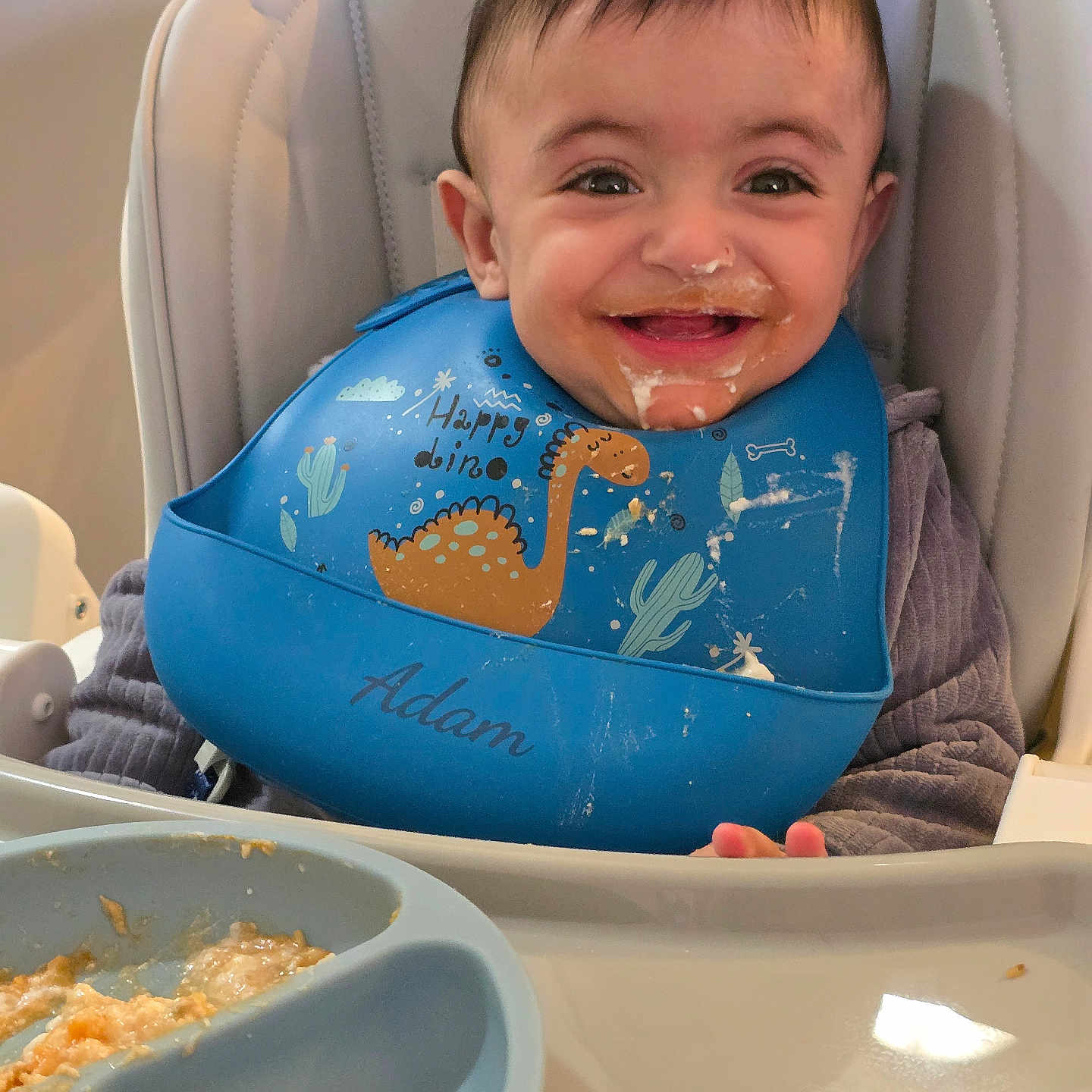 Adam joined the competition — help win amazing prizes! baby, bib, child, clothing, cute, dinosaur, face, feeding, food, happy, high_chair, indoor, infant, meal, messy, person, plate, smiling, tongue_out, young