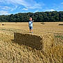 Giovanni participe au concours pour gagner de l'argent avec cette photo : child, boy, hay_bale, field, wheat, outdoor, nature, sky, clouds, forest, summer, sunny, casual_clothing, pointing, standing, smiling, shorts, shoes, grass, rural