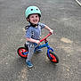 child, toddler, helmet, balance_bike, bike, pavement, street, sidewalk, car, parking, shoes, clothing, shorts, tshirt, outdoor, smile, grin, play, active, person