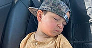 Jaylen is registered to the contest to win money with this photo: child, sleeping, car, backseat, baseball_cap, camo, yellow_shirt, leather_seat, seatbelt, window, sunlight, nap, relaxed, young_boy, casual_clothing, portrait, indoors, peaceful, headwear, kid