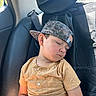 child, sleeping, car, backseat, baseball_cap, camo, yellow_shirt, leather_seat, seatbelt, window, sunlight, nap, relaxed, young_boy, casual_clothing, portrait, indoors, peaceful, headwear, kid