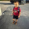 Jaylen is registered to the contest to win money with this photo: child, boy, backpack, red_tshirt, shorts, brown_shoes, asphalt, truck, parking_lot, daylight, outdoor, smiling, standing, casual_clothing, vehicle, fence, tree, house, sidewalk, sunlight
